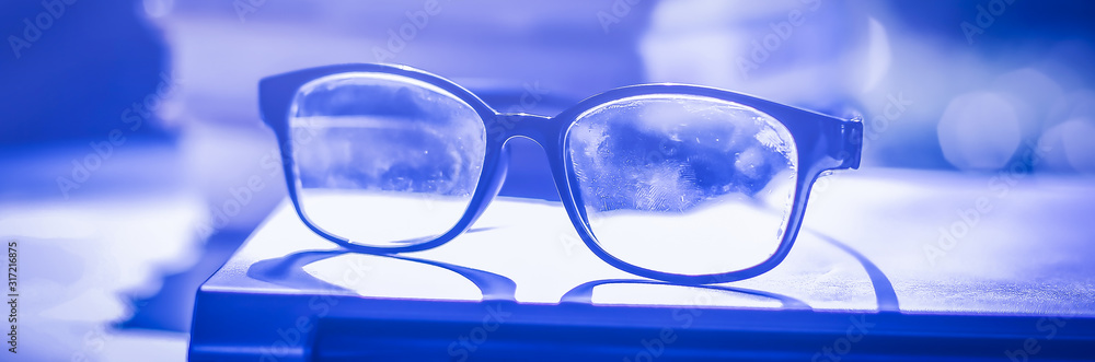 Poster stack of books with glasses placed on the open book in library.