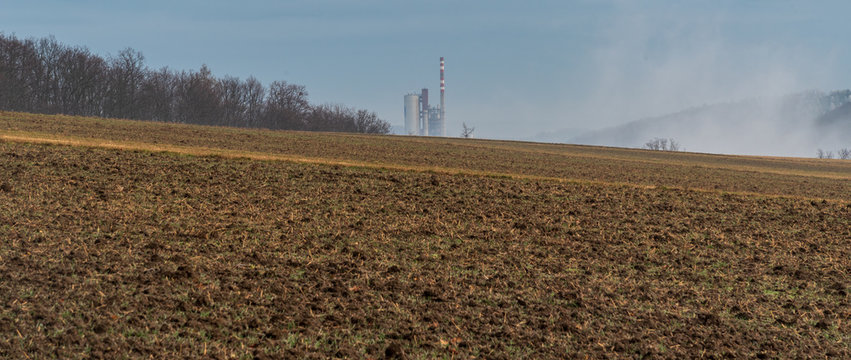 field with forest around and factory on the background