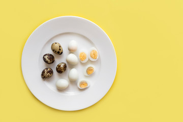 Group, set of peeled and unpeeled small organic quail eggs, whole cut in halves, halved boiled versus raw on a white plate on yellow background. Top view from above. Before cooking and after. Egg yolk