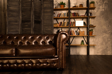 Brown leather sofa in an interior room with a bookcase. © vfhnb12