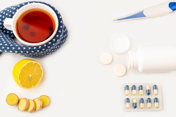 Cup of tea, ginger, lemon and alternative remedies and traditional pills on blue, copy space for text, top view. The concept of seasonal diseases and treatment of colds, flu, heat. Prevention of virus