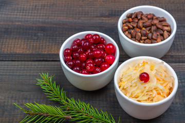 Sauerkraut or fermented cabbage with cranberries and pine nuts on rustic wooden background. The concept of healthy eating. Organic and vegetarian food, fermentation ingredients. Close up, copy space 
