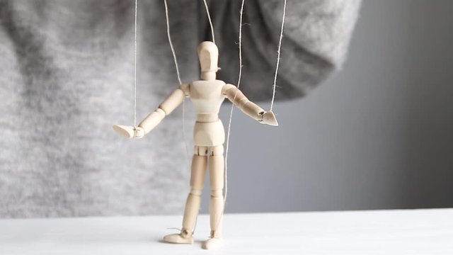 Female hands control a wooden man model toy using threads on a gray background. Business control over subordinates