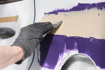 Body shop for car repair. A mechanic spackles a damaged part of a car after an accident.