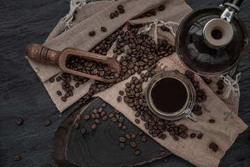 Fototapeta na wymiar Coffee style, Cup of coffee and coffee beans roating with old wooden scoop and coffee beans around on the wooden and dark stone background.
