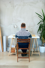 Back view of an Attractive freelance male sitting in modern office and typing on notebook.