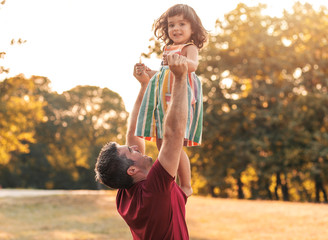 Happy father playing and carrying his daughter in park.