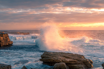 Huge wave crushing over rock with splashes of white foam at sunrise