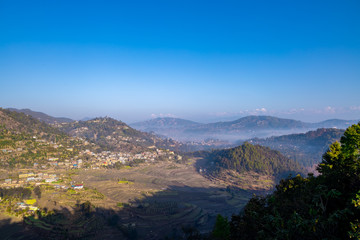 Moody Dramatic view of hills covered in fog and Great Himalaya Range in the backdrop. Terrace farming