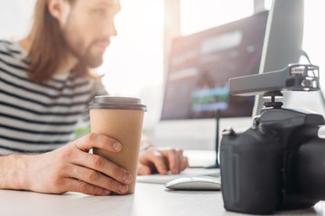selective focus of editor holding paper cup and looking at computer monitor