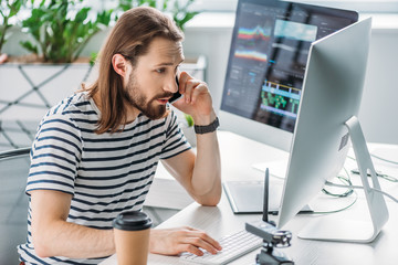 bearded art editor talking on smartphone near computer monitors