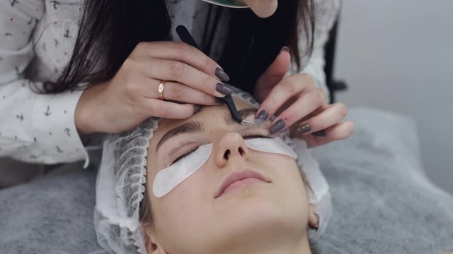 A lash maker is sticking a lift pad on an eye. The master is using the tweezers. The client is prepared for the lash lamination.