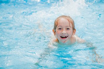 Fototapeta na wymiar Funny portrait of happy cute little girl in swimming pool. Child learn to swim. Summer holiday and healthy lifestyle concept