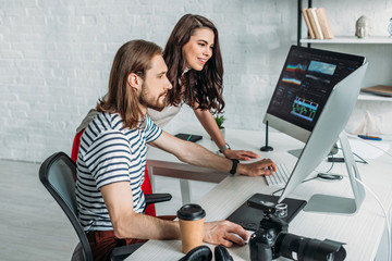 happy art editor looking at computer monitor near coworker