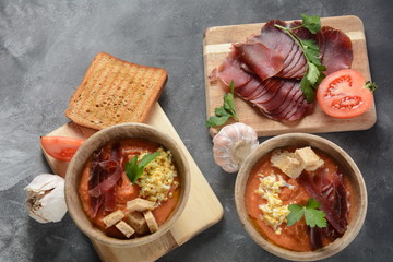 Traditional Spanish andalusian tomato cream soup Salmorejo served with egg, ham jamon, bread in woooden bowl. Summer cold soup concept
