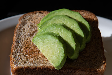 Slices of fresh avocado on one wholemeal toast  in front of black background. Close up avocado on toast. Low key photograph. Selective focus.