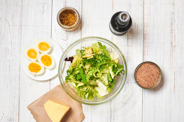 Making a salad of a mix of fresh vegetables and chicken eggs, tuna, mustard, cheese on a white wooden background. Healthy and wholesome organic food, diet, proper nutrition concept.