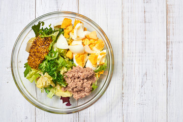 Making a salad of a mix of fresh vegetables and chicken eggs, tuna, mustard, cheese on a white wooden background. Healthy and wholesome organic food, diet, proper nutrition concept.