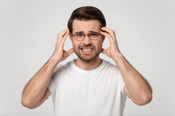 Upset young man in eyeglasses suffering from sudden strong headache.