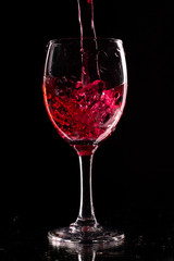 a wine glass on a dark background is filled with a red drink.