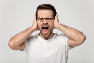 Close up headshot portrait young stressed man covering ears.