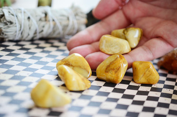 Woman's hand holding yellow jasper healing crystals. Tumbled yellow crystals, natural lighting and lush color. Intricate yellow swirls on beautiful jasper, witches healing stone. Wiccan alter magic