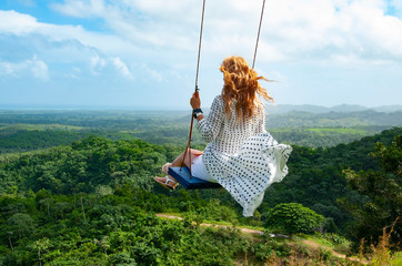 Blond woman in white dress swinging on the top of the mountain in Dominican Republic