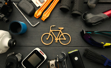 A lot of different bicycle accessories lying on wooden table around a little bicycle icon