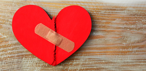 Two parts of red broken wooden heart taped by a patch. Concept of the forgiveness, renewal of...