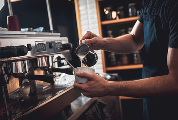 Barista preparing cappuccino on espresso machine for customer in coffee shop.