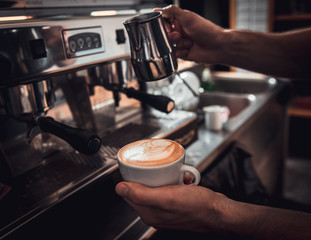 Fototapeta na wymiar Close up of barista hands preparing cappuccino on espresso machine for customer in coffee shop.
