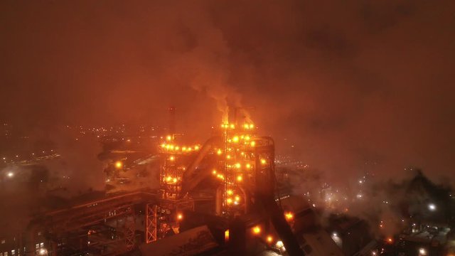 Aerial view of metallurgical plant blast furnace at night with smokestacks and fire blazing out of the pipe. Industrial panoramic landmark with blast furnance of metallurgical production