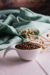 Fototapeta na wymiar Seeds of brown flax in a white ceramic spoon on a background of pale green fabric. Still life