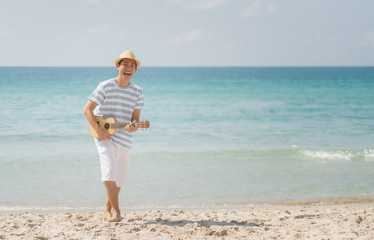 Asian man playing a ukulele and singing with enjoy on a tropical beach, Live life happily on holidays.