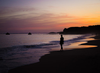 Portugal, Algarve, The best beaches of Portimao, Praia da Rocha, lilac golden sunset over the waves of The Atlantic Ocean, a girl walking the waves, silhouette happy woman at sunset on the beach