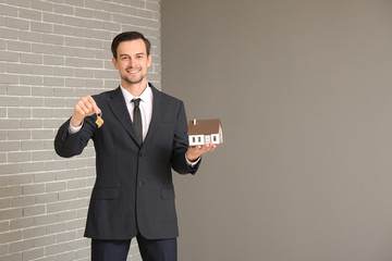 Portrait of male real estate agent with key and model of house indoors