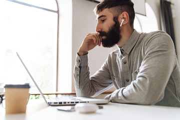 Fototapeta premium Photo of thinking young man using laptop and earpods while sitting