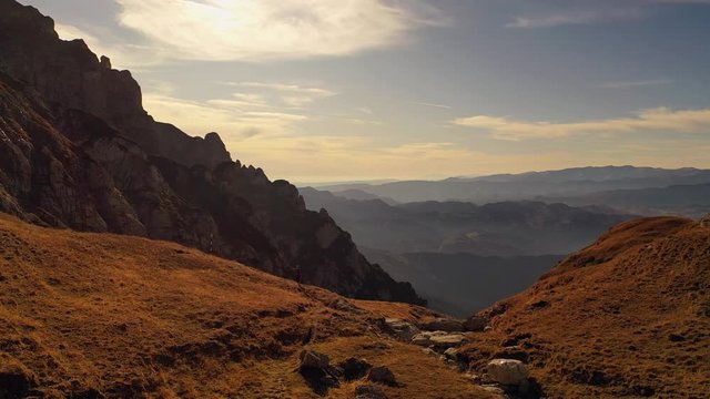 4k drone clip with hiker trekking on a huge mountain valley in Bucegi mountains, during magical golden hour light in autumn season in Romania