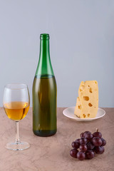 front view of the glass, a bottle of wine, grapes and cheese on a wooden table.