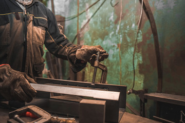 Man clamps iron products into c-clamps. Man works with clamps. Steel workshop concept