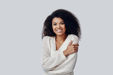 Attractive young African woman smiling and looking at camera while standing against grey background