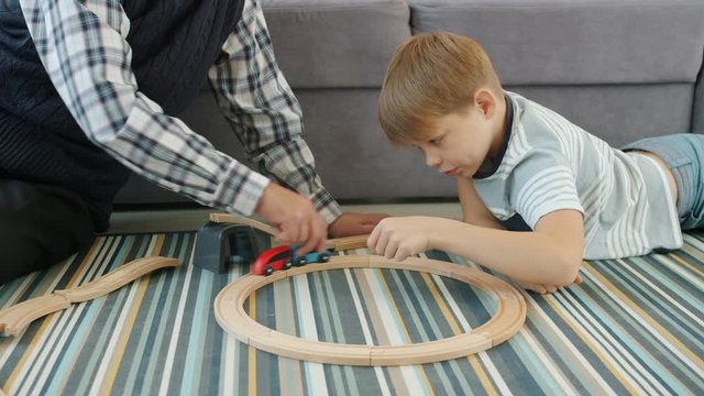Joyful kid is playing toy cars with caring senior grandfather relaxing on floor in apartment. Happy childhood, entertainment and casual life concept.