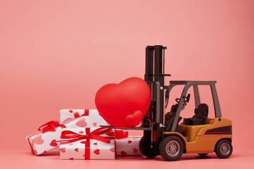 Forklift, red heart and gift boxes on pink background. Valentine's Day.