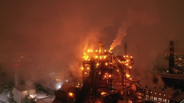 Aerial view of  steel plant at night with smokestacks and fire blazing out of the pipe. Industrial panoramic landmark with blast furnance of metallurgical production. Concept of environmental pollutio