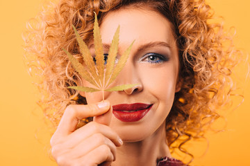 Portrait of a curly woman with a leaf of marijuana in her hand. Face close-up on a yellow...