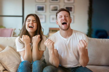 young couple man and woman sitting on the sofa both looking winning, grimacing mood