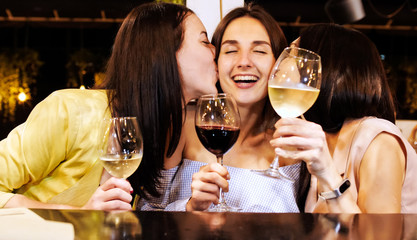 Three pretty girls are laughing during look over photos on phones at the bar