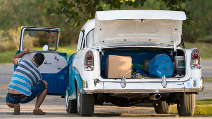 back of a cuban classic car with an open trunk and a man kneeling next to the car