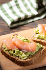 Bruschetta with avocado and salmon on a wooden Board on a brown wooden table. Toasted bread with avocado and red fish. The concept is useful and delicious Breakfast