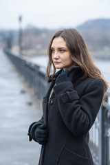 A brunette girl in a black coat is walking on a cold winter day without snow. Portrait of a girl.